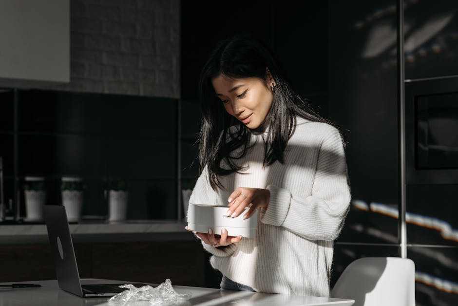 East Asian woman unpacking a package indoors, with natural lighting creating shadows on her white knitted sweater.
