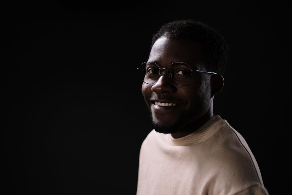 Close-up portrait of a smiling man wearing glasses against a dark background.