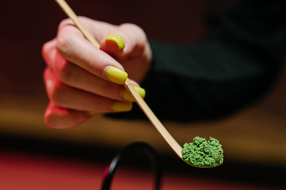 A detailed shot of a hand holding green tea powder on a spoon, showcasing a traditional tea ceremony.