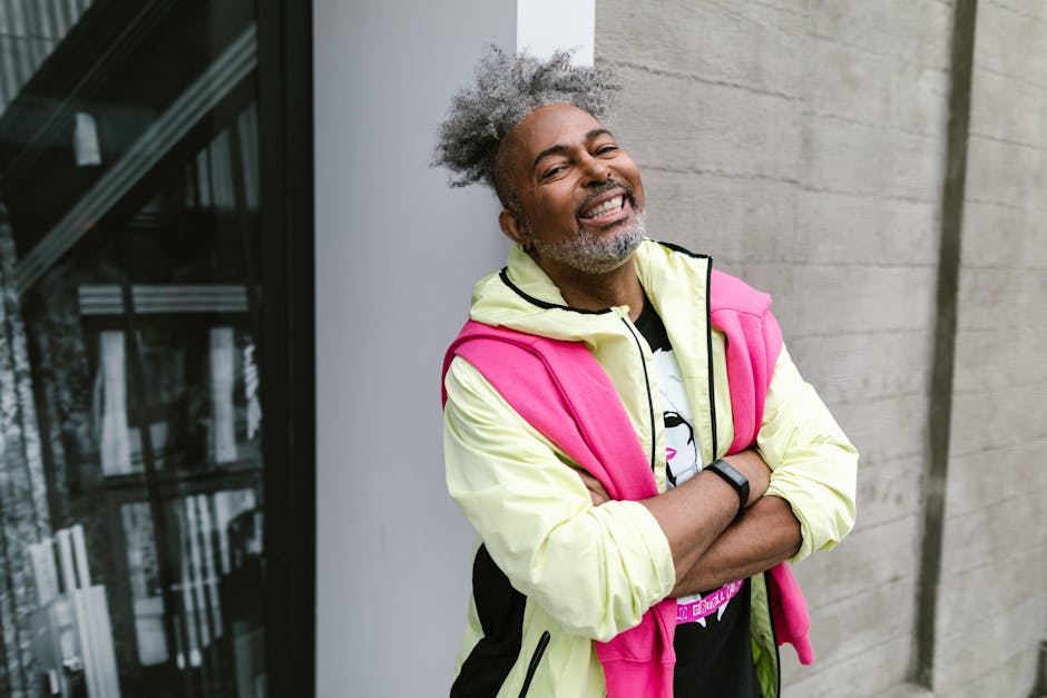 Elderly man with afro hair and stylish outfit smiling outdoors.