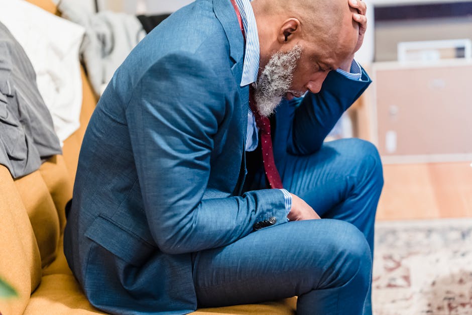 A concerned mature businessman in a blue suit sits indoors appearing stressed and worried.