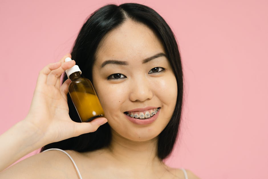 Portrait of a smiling woman with braces holding a cosmetic bottle against a pink background.
