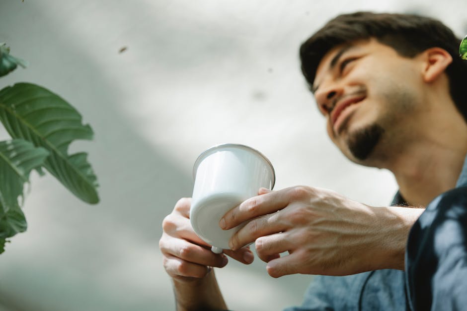 Cheerful young man savoring a hot beverage in a sunny outdoor setting, surrounded by greenery.