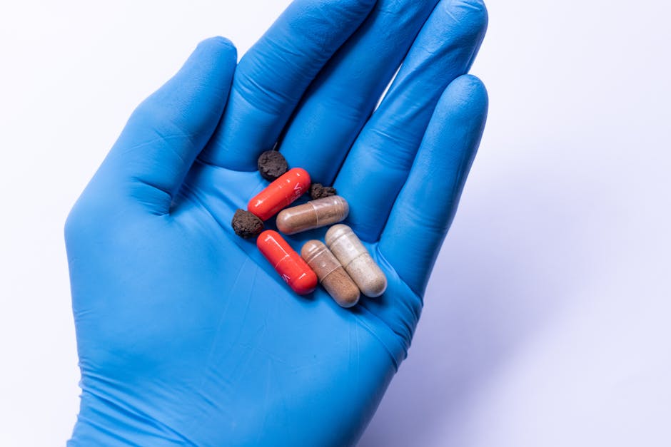 Close-up of various pills in a blue gloved hand, set against a white background.