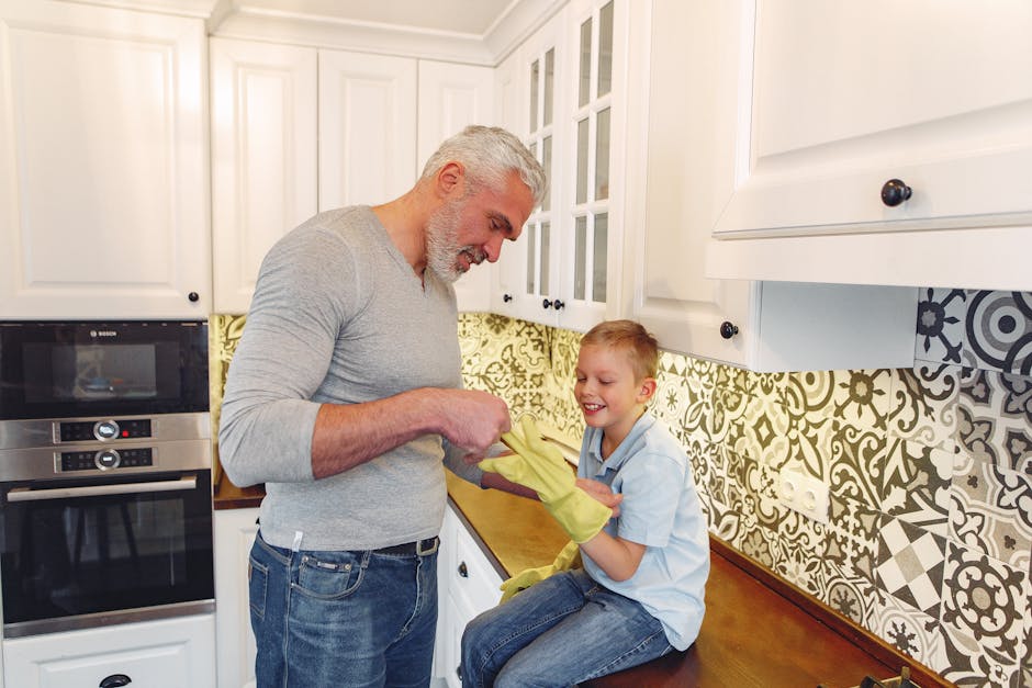 Side view of satisfied grey haired father with beard and smiling kid at kitchen