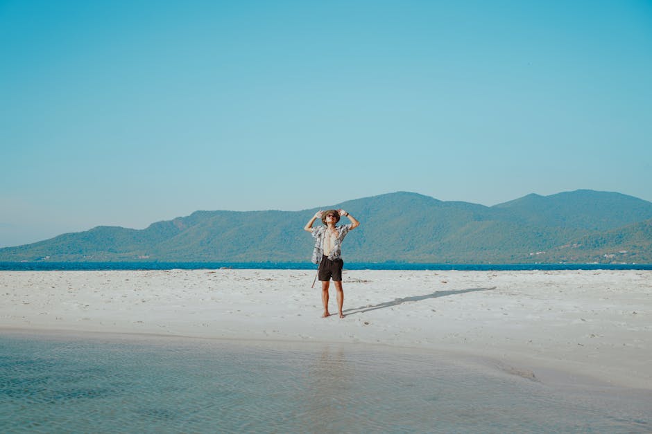 Young man enjoying a sunny day on a serene tropical beach with mountain views.