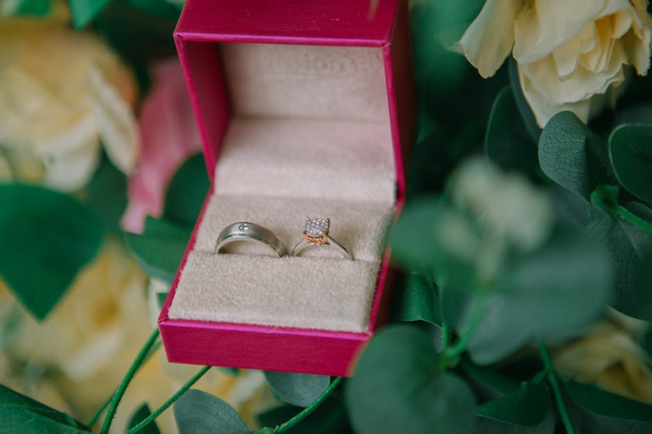 Close-up of wedding rings in a pink velvet box surrounded by green leaves.