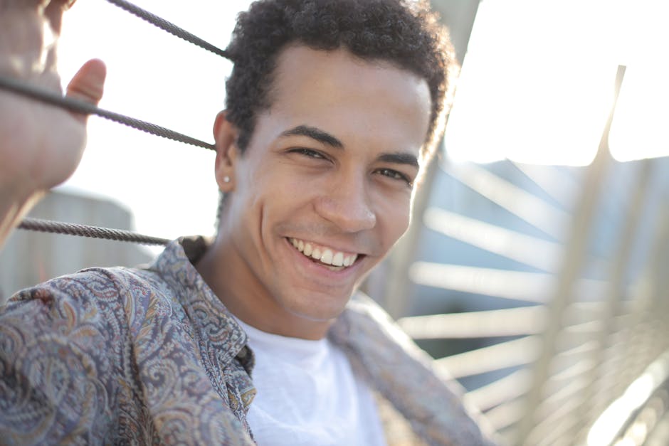 Cheerful young man smiling outdoors on a sunny day in a city setting.