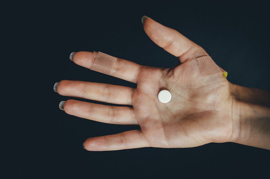 A hand with adhesive bandages holds a tablet against a dark background, highlighting injury and medication.