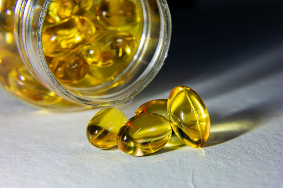 Close-up of golden softgel capsules spilled from an open bottle on a white surface.