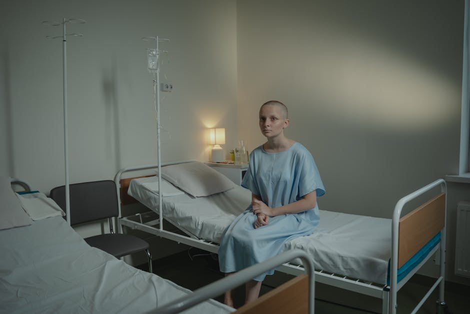 A woman in a hospital gown sits alone in a dimly lit hospital room, reflecting on her situation.