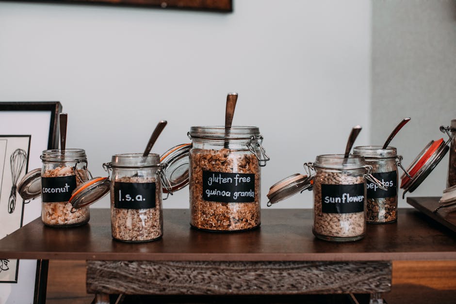 Close-up of labeled glass jars containing various grains and seeds on a wooden table.