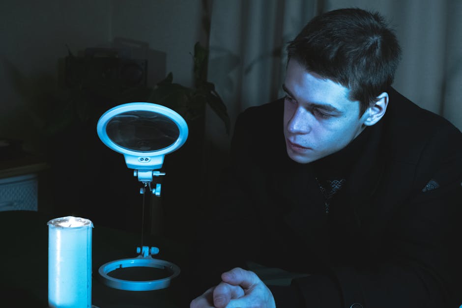 A man in a black suit sitting indoors, illuminated by a lamp and candlelight.