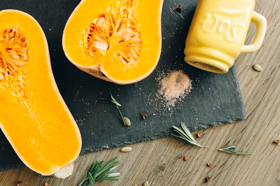 A close-up shot of halved butternut squash with rosemary sprigs and salt on slate.
